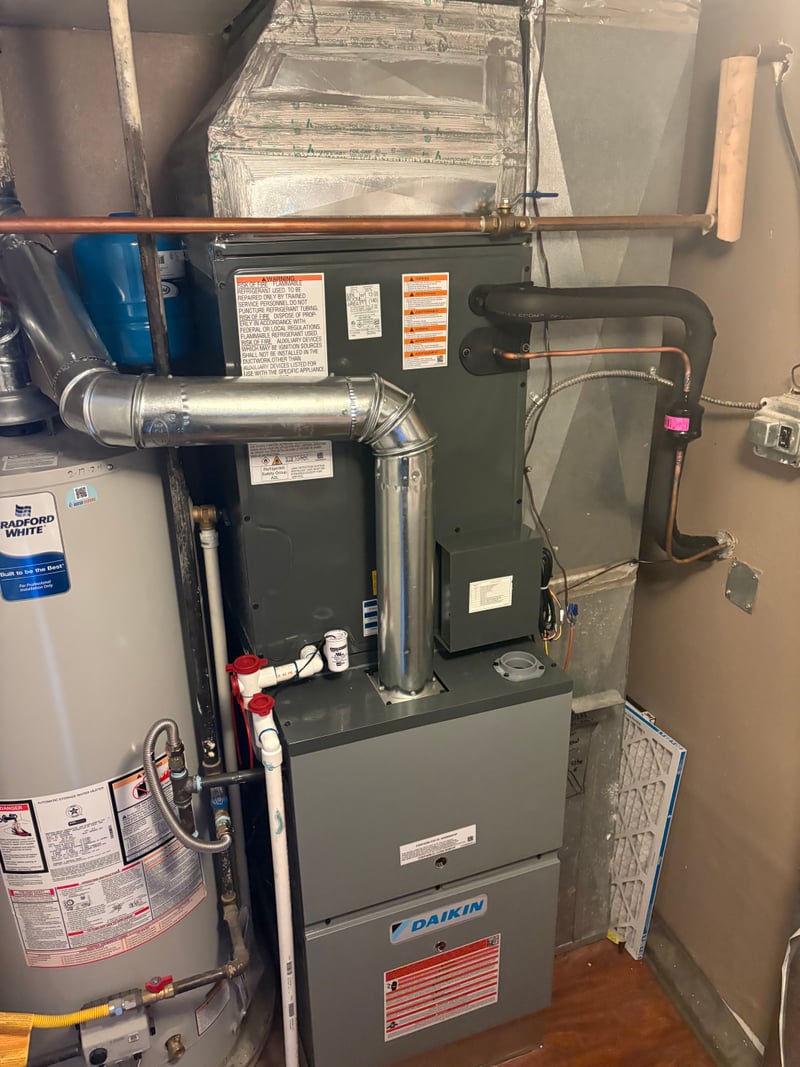 Daikin outdoor heat-pump unit installed on a pad behind a residential back patio and privacy fence.