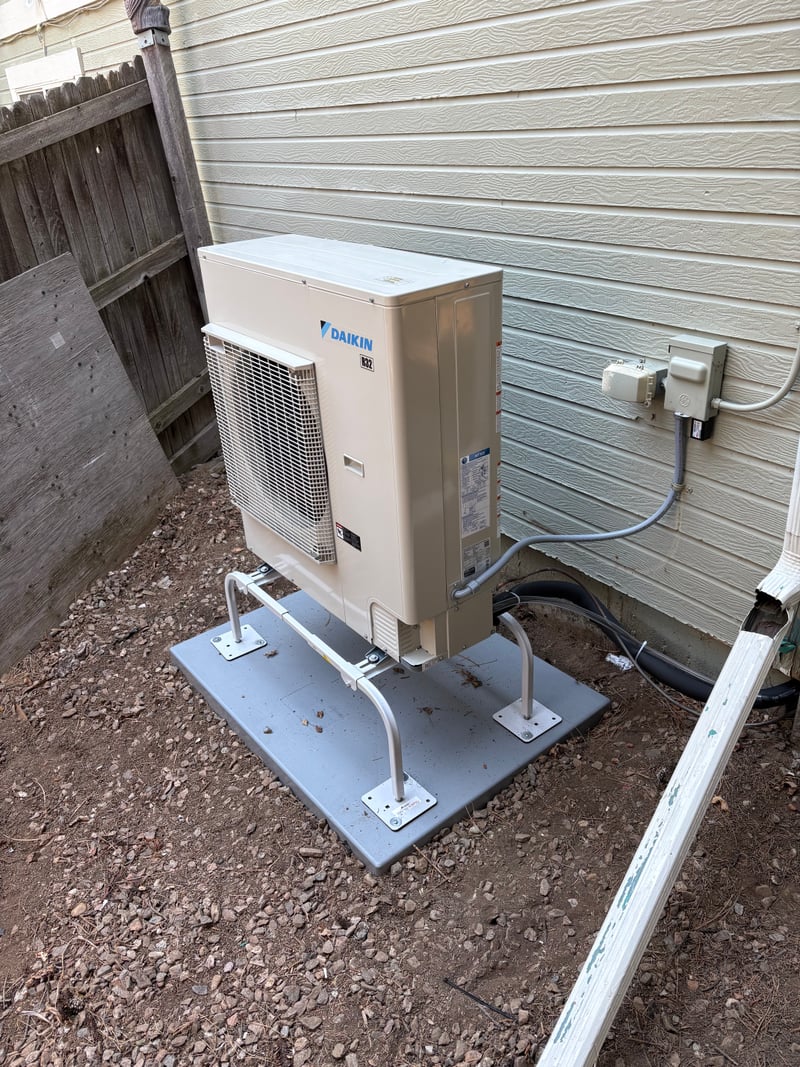 Daikin outdoor heat-pump unit installed on a composite ground pad next to a fenced back yard.
