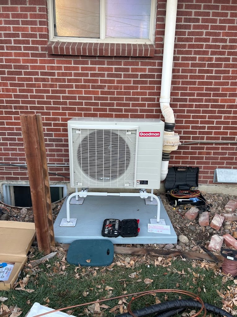 Newly installed Goodman mini-split outdoor unit mounted on a stand against a red-brick home exterior.