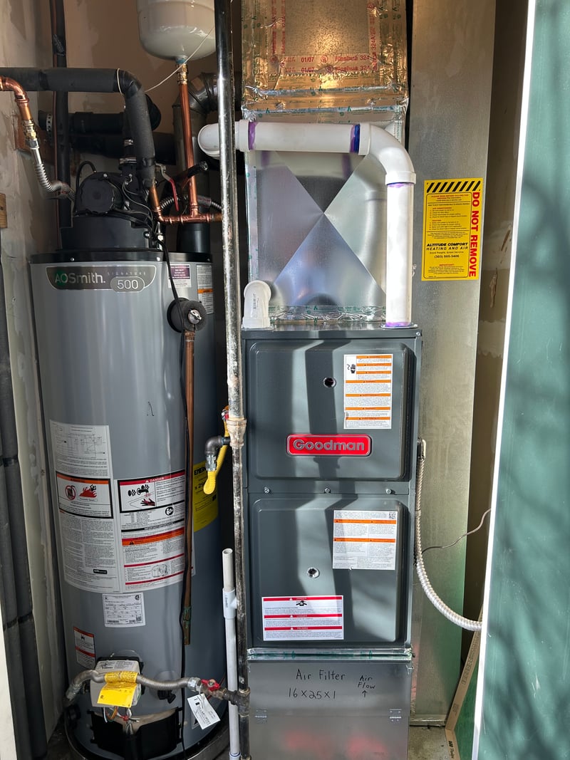 Newly installed Goodman gas furnace and AO Smith water heater arranged side-by-side in a residential utility closet.