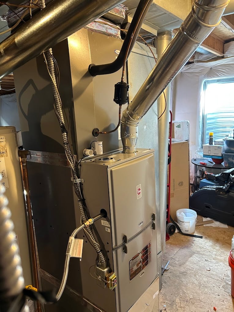 Newly installed Rheem gas furnace with reworked galvanized supply and return ductwork in a basement mechanical room.
