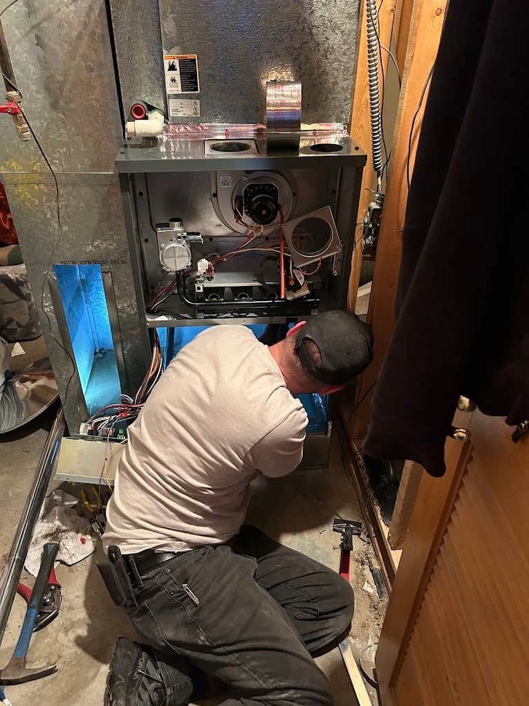 Colorado Bear technician kneeling in front of an opened furnace cabinet, diagnosing internal components during a service call.