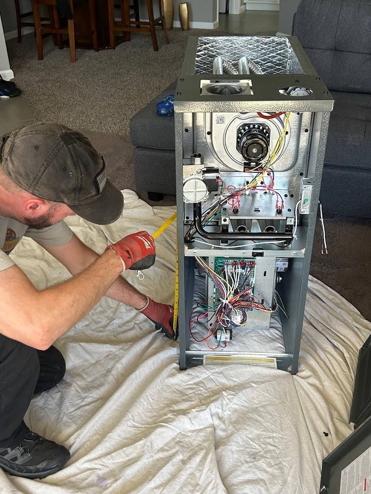 Colorado Bear installer measuring a new gas furnace laid on a drop cloth in a living room during a replacement install.